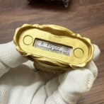 Gold-tone Zippo lighter bottom with serial No. 02157, Bradford, PA, Made in USA, held by a gloved hand.