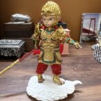 Gold-painted monkey-warrior figurine in ornate armor, standing on a white cloud pedestal and gripping a red staff.