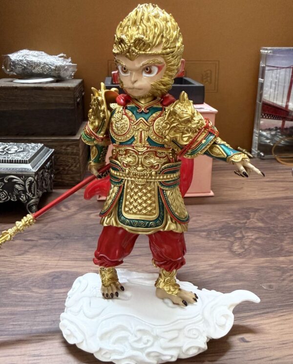 Gold-painted monkey-warrior figurine in ornate armor, standing on a white cloud pedestal and gripping a red staff.