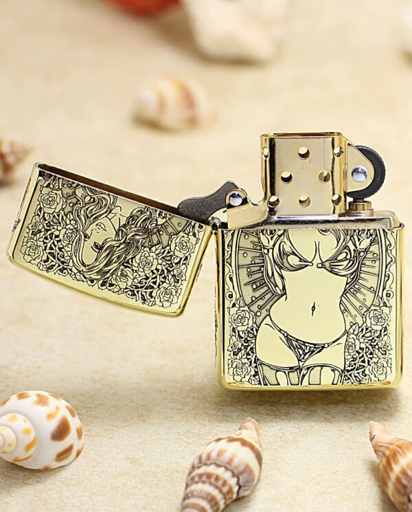KZ365-02 Gold engraved lighter on a sandy beach with seashells, lid open, featuring a bikini-clad woman and floral details in black and gold.
