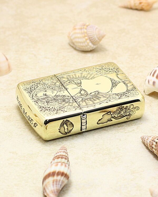 KZ365-04 Gold Zippo lighter with ornate floral and figure engraving, set on sand among seashells.