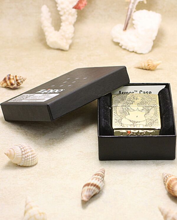 KZ365-06 Gold engraved lighter in an open black box on a sandy beach with seashells nearby (presentation or product shot). -or- A gold-engraved lighter displayed in its black box on a beach-themed surface.