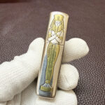 Gold-tone decorative accent detail within the engraved Egyptian pharaoh design
